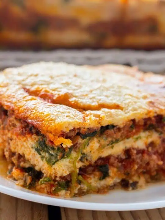 A slice of Whole30 lasagna on a white plate showing layers of eggplant noodles, rich meat sauce, and golden cashew cream.