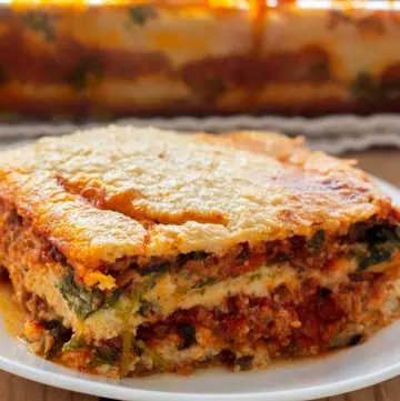 A slice of Whole30 lasagna on a white plate showing layers of eggplant noodles, rich meat sauce, and golden cashew cream.