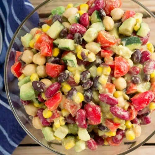 Canned bean salad in a glass bowl next to a blue napkin and spoon on a wooden table.