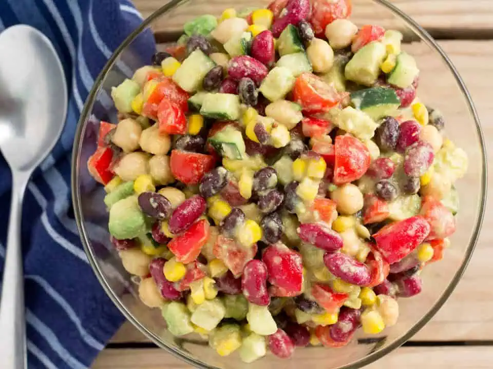 Canned bean salad in a glass bowl next to a blue napkin and spoon on a wooden table.