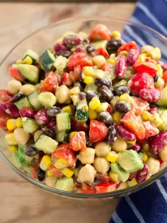 Canned bean salad in a glass bowl next to a blue napkin on a wooden table.