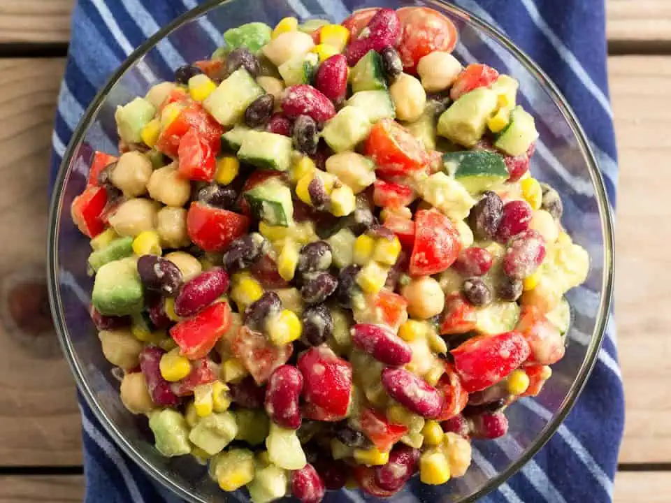 Canned bean salad in a glass bowl on top of a blue napkin on a wooden table.