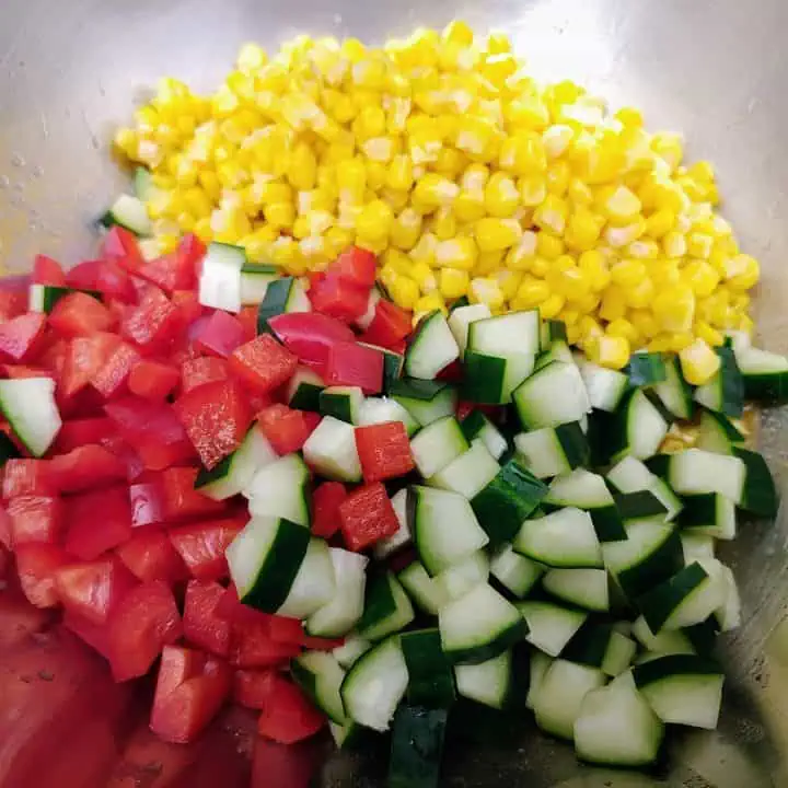 Large bowl filled with diced cucumbers, red bell peppers, and canned corn.