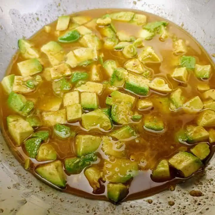 Diced avocados in lime dressing in large stainless steel bowl.