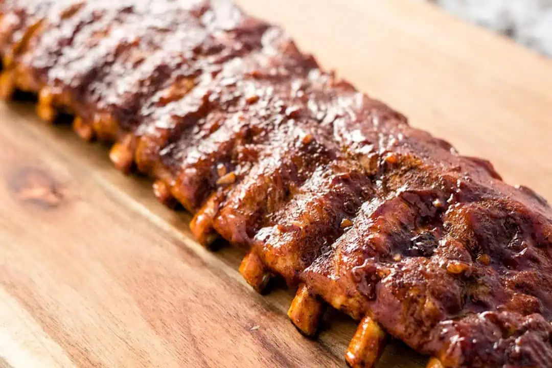 One rack of saucy baby back ribs on a wooden cutting board.