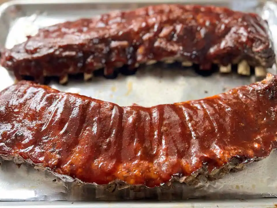 Two racks of saucy baby back ribs on a baking sheet lined with aluminum foil.