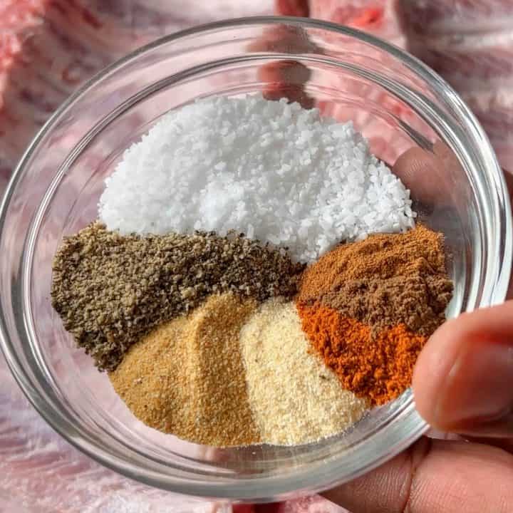 Holding spices for dry-rubbed baby back ribs in a small glass bowl with ribs in the background.