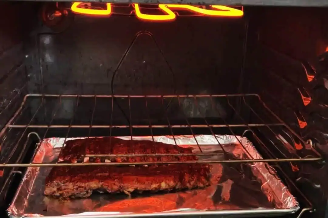 Baking sheet with two racks of baby back ribs on lowest rack of oven with a high broiler.