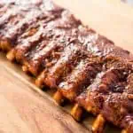 One rack of saucy baby back ribs on a wooden cutting board.