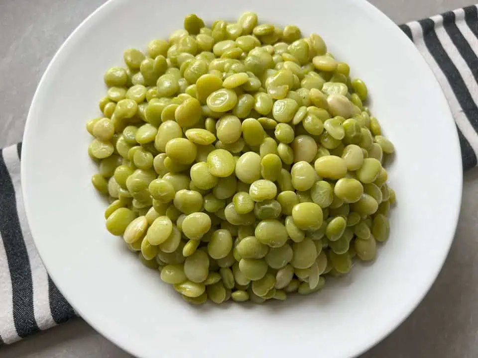 White bowl full of baby lima beans on top of a black and white striped napkin.