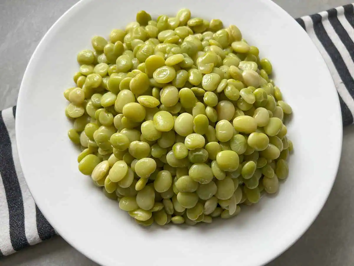 White bowl full of baby lima beans on top of a black and white striped napkin.