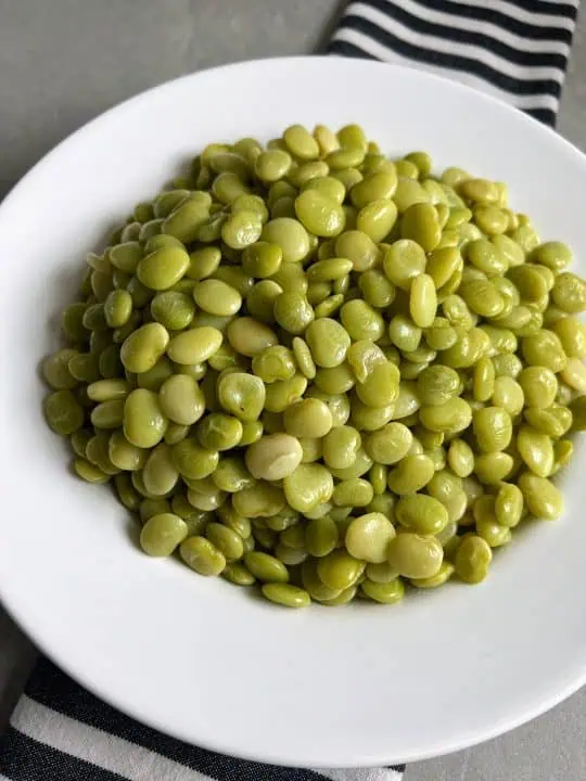 White bowl full of baby lima beans on top of a black and white striped napkin.