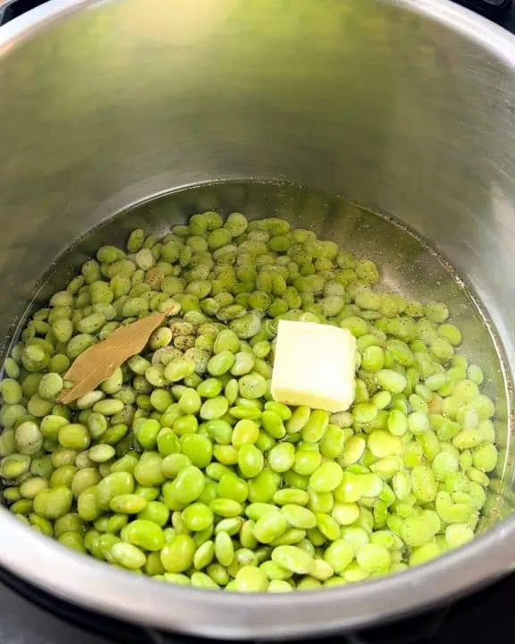 Frozen baby lima beans in an Instant Pot with water, butter, and bay leaf.