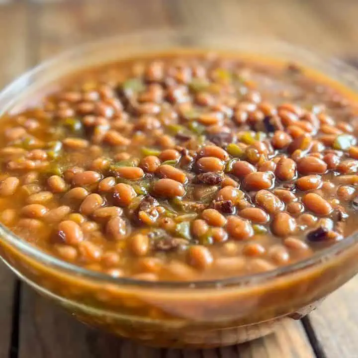 Glass bowl full of baked beans on a wooden table.