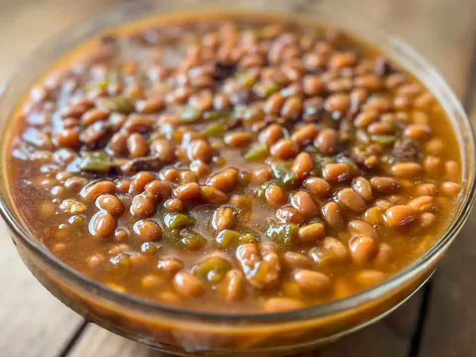 Glass bowl full of baked beans on a wooden table.