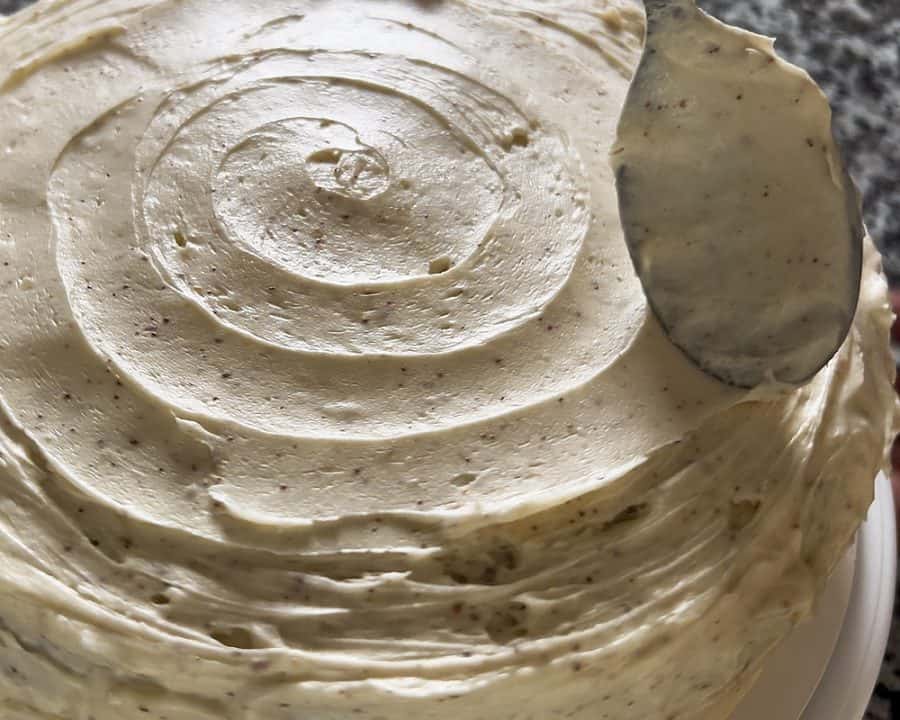 A spoon swirling brown butter cream cheese frosting on top of a layered cake.