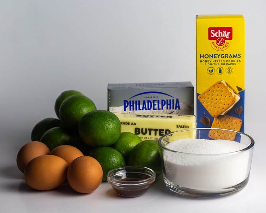 Ingredients for gluten-free key lime bars including fresh limes, eggs, butter, sugar, vanilla, Philadelphia cream cheese, and Schär Honeygrahams