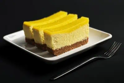 Side view of key lime bars with visible layers of crust, cheesecake, and lime topping, served on a modern square plate