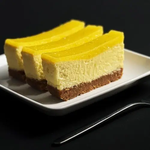 Side view of key lime bars with visible layers of crust, cheesecake, and lime topping, served on a modern square plate