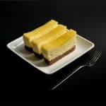 Square image of three gluten-free key lime cheesecake bars arranged on a white plate with a fork on the side