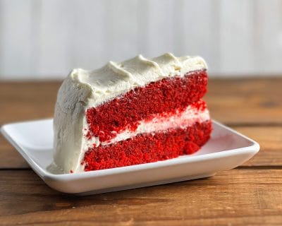 Gluten-free red velvet cake slice with cream cheese frosting on a white plate