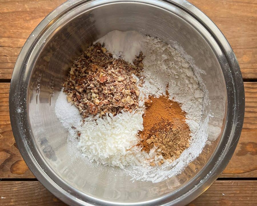 Bowl of flour, pecans, shredded coconut, baking soda, and spices for carrot cake