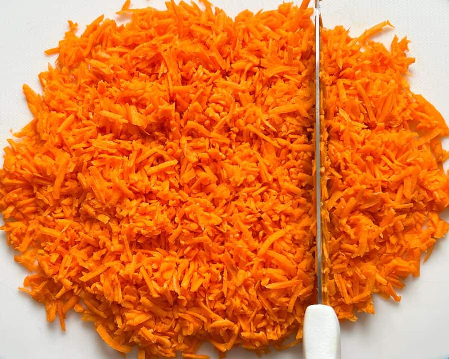 A knife cutting a pile of freshly shredded carrots on a white cutting board