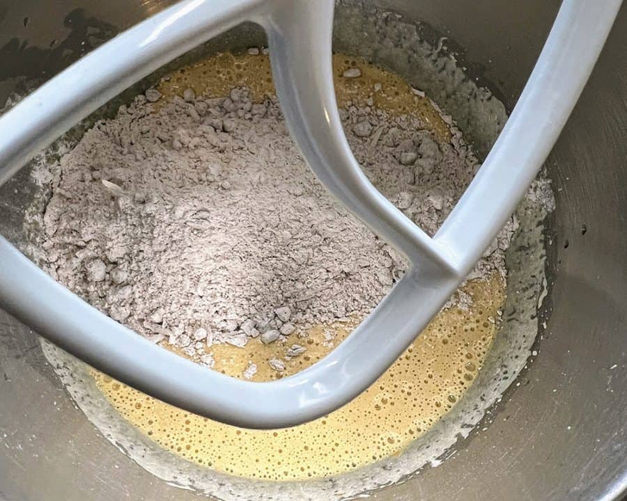 Mixer bowl with dry ingredients being added to the wet batter using a paddle attachment