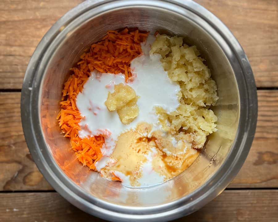 Bowl containing shredded carrots, crushed pineapple, applesauce, and buttermilk before mixing