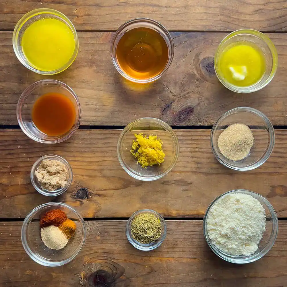 Overhead of small bowls with butter, honey, hot sauce, lemon zest, garlic, spices, and Parmesan for Nashville hot, lemon-pepper honey, and garlic-Parmesan finishes.