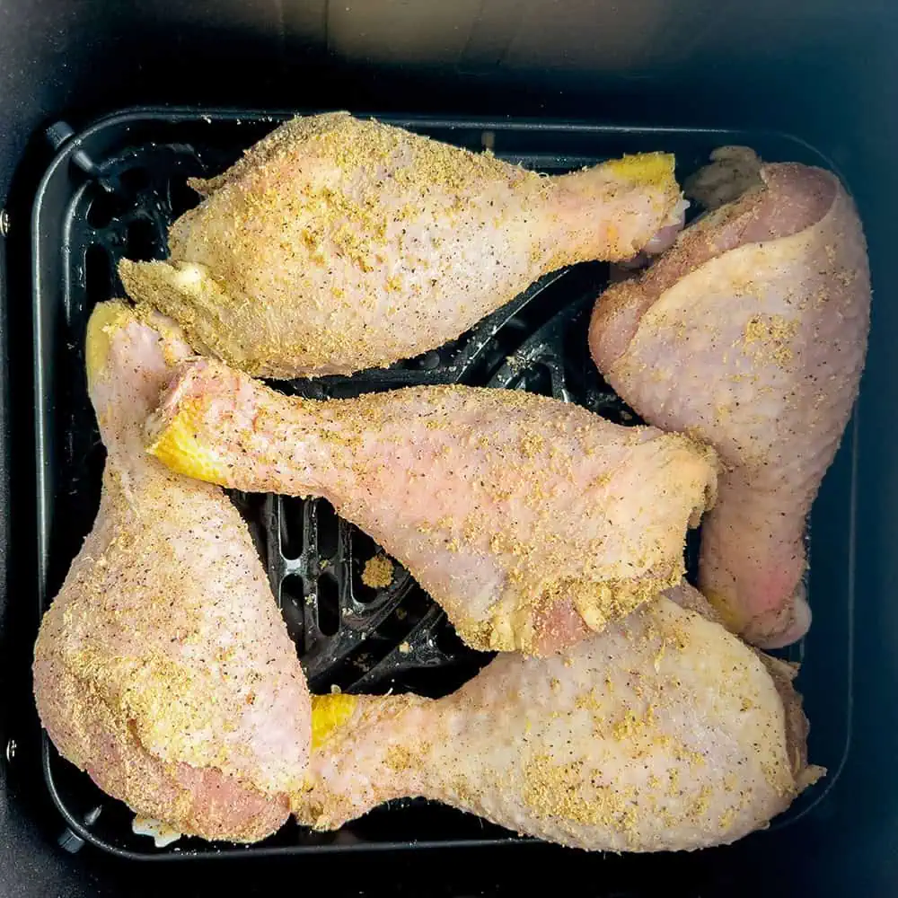 Seasoned drumsticks arranged in the air fryer basket with space between pieces.