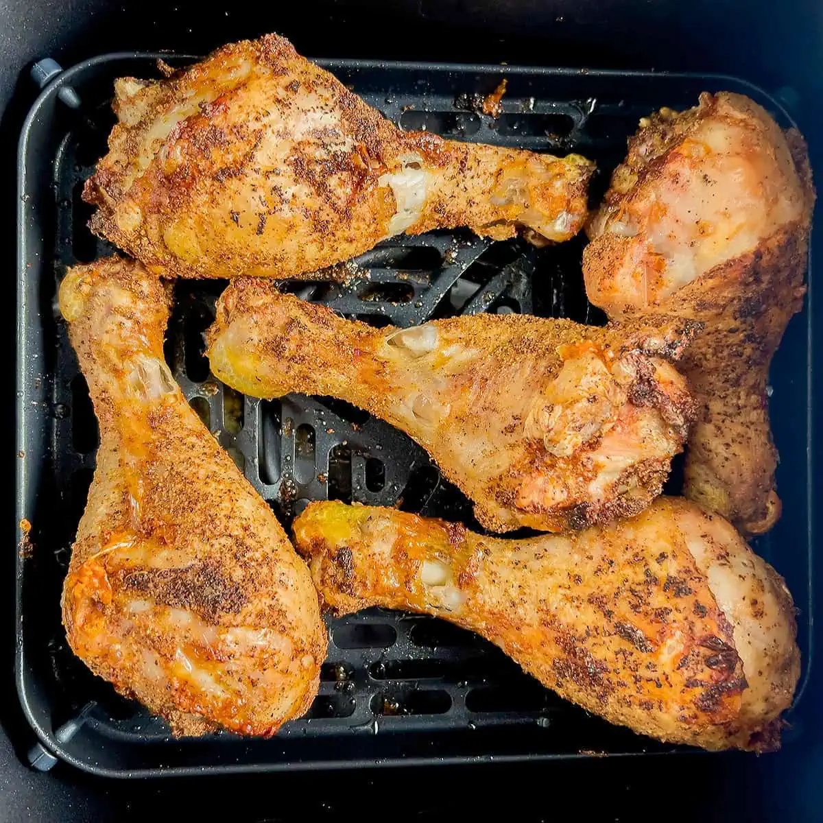 Cooked drumsticks in the air fryer basket with browned, crisp skin.