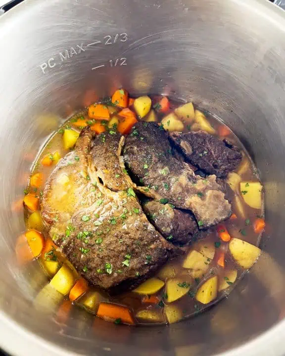 Chuck roast in an Instant Pot surrounded by carrots, potatoes, and parsley garnish, showing pot's max fill line.