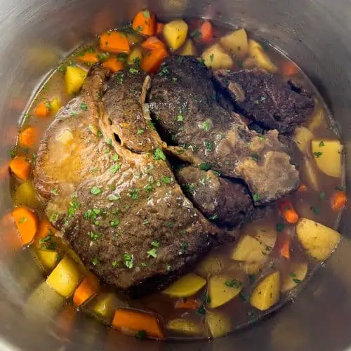 Chuck roast in an Instant Pot surrounded by carrots, potatoes, and parsley garnish, showing pot's max fill line.