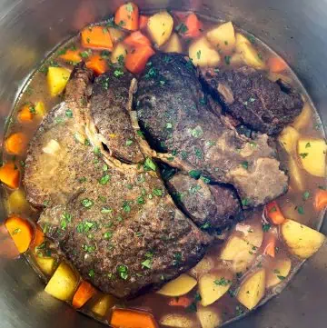 Instant Pot filled with cooked chuck roast, carrots, and potatoes in broth, garnished with parsley.
