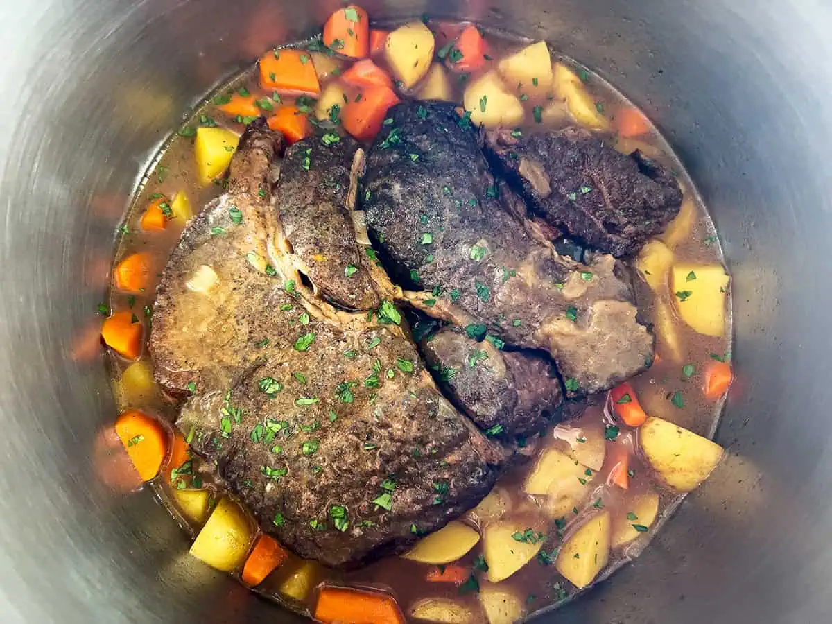 Instant Pot filled with cooked chuck roast, carrots, and potatoes in broth, garnished with parsley.
