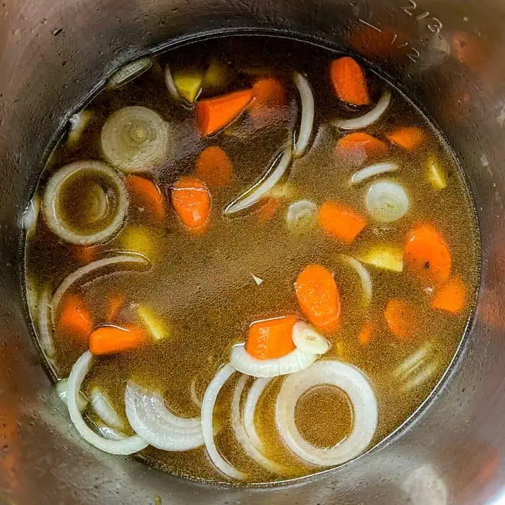 Sliced onions and carrots in beef broth inside an Instant Pot, just before final pressure cook.