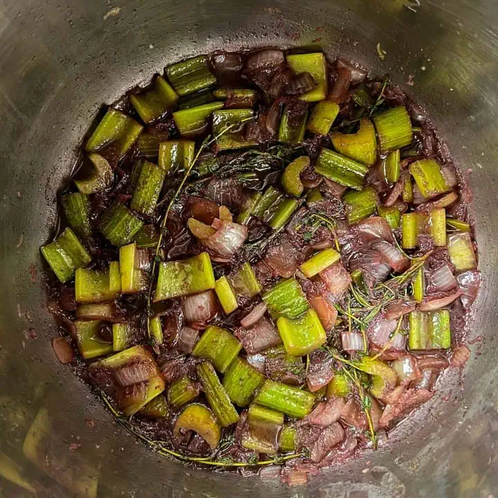 Celery, onion, garlic, and herbs simmering in red wine inside an Instant Pot.