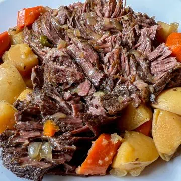 Shredded pot roast with carrots and potatoes on a serving plate, covered in rich gravy.