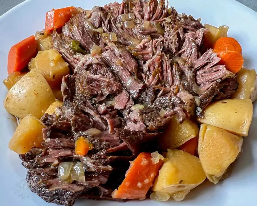 Shredded pot roast with carrots and potatoes on a serving plate, covered in rich gravy.