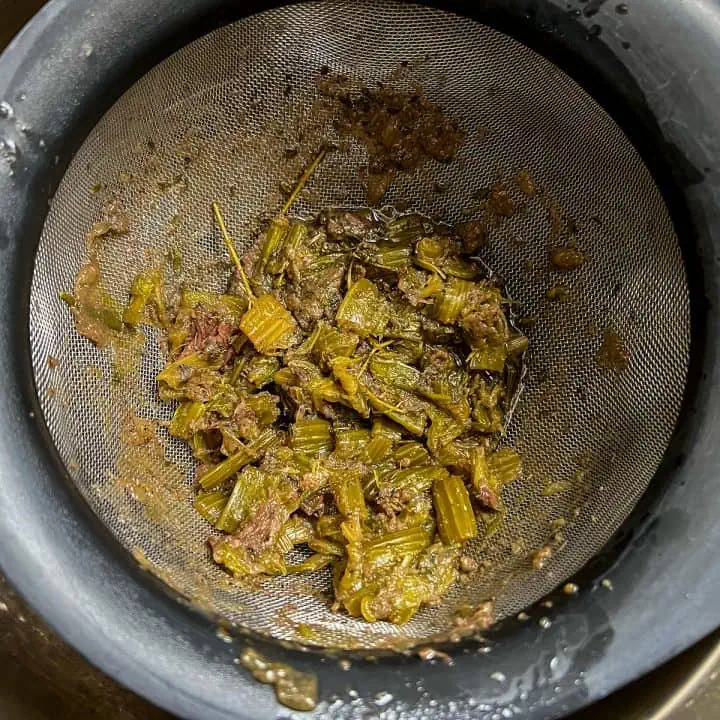 Used aromatics, herbs, and celery caught in a fine mesh strainer after cooking pot roast in the Instant Pot