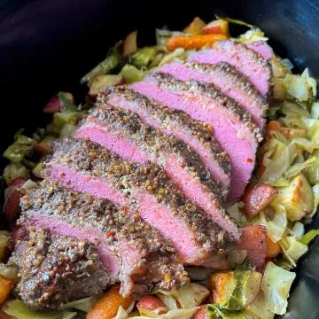 Close-up of sliced corned beef brisket with peppercorn crust on cabbage, carrots, and potatoes