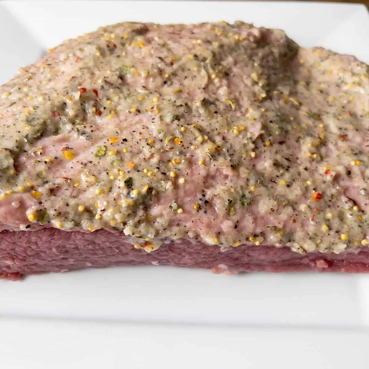 Corned beef brisket coated in the seasoning paste on a white plate.
