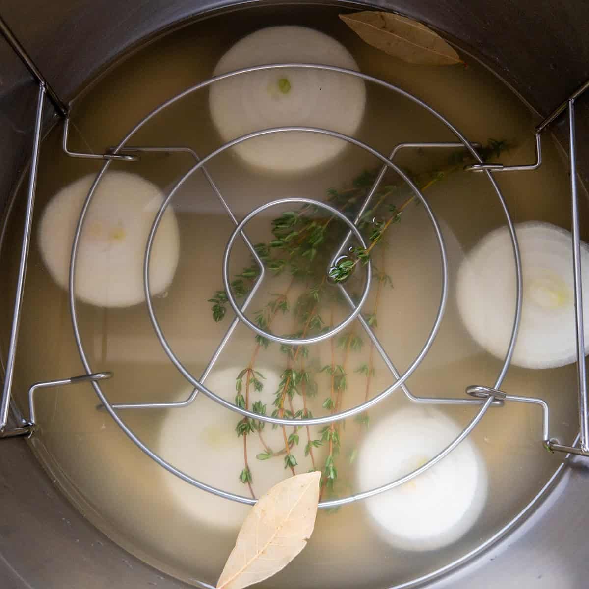 Instant Pot with trivet, chicken broth, onion halves, thyme, and bay leaf.