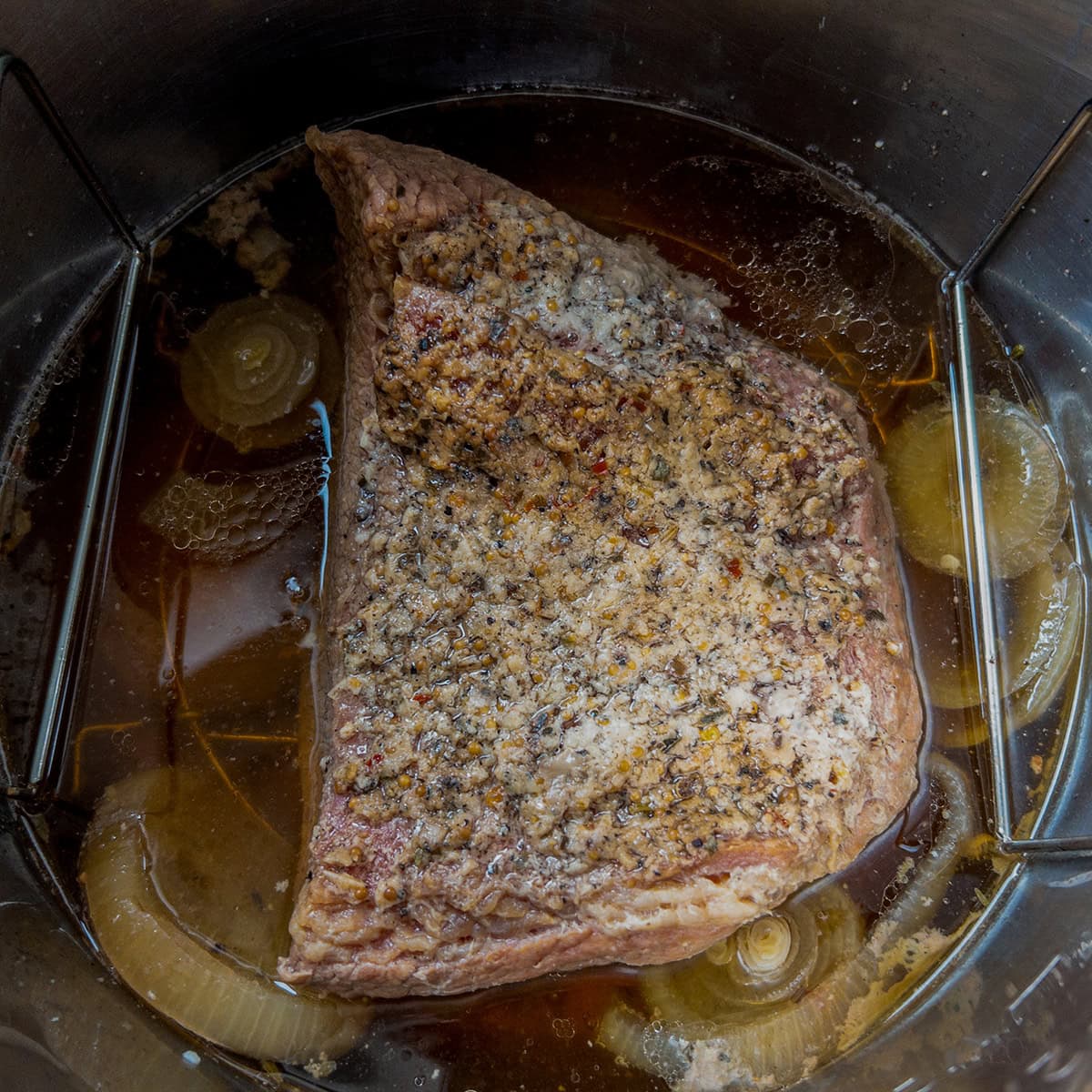 Cooked corned beef brisket in the Instant Pot with chicken broth, onions, and seasoning on top before broiling.
