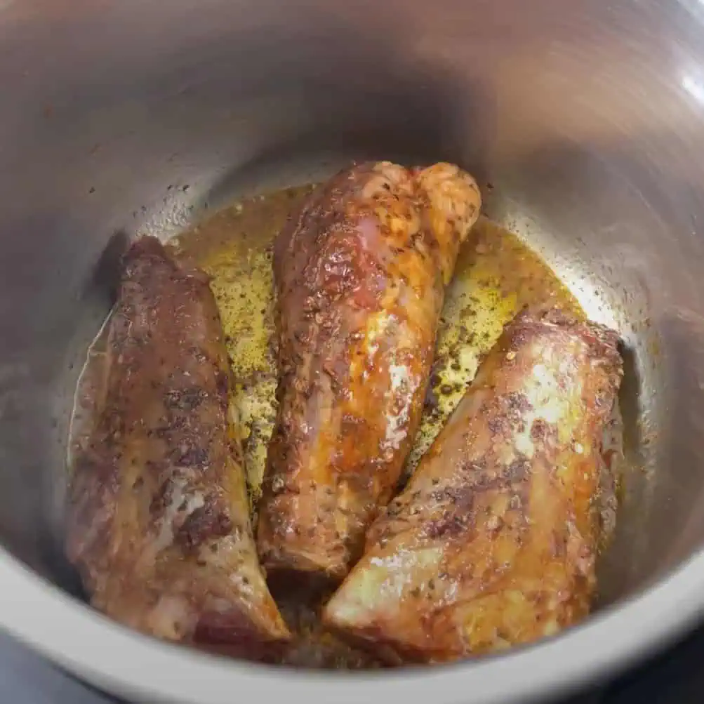 Lamb shanks browning in the Instant Pot insert with oil and seasoning for color and flavor.