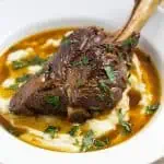 Close-up of a pressure cooker lamb shank over creamy mashed potatoes with rich gravy and chopped parsley.
