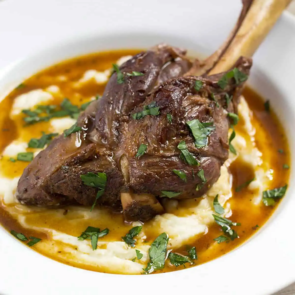 Close-up of a pressure cooker lamb shank over creamy mashed potatoes with rich gravy and chopped parsley.