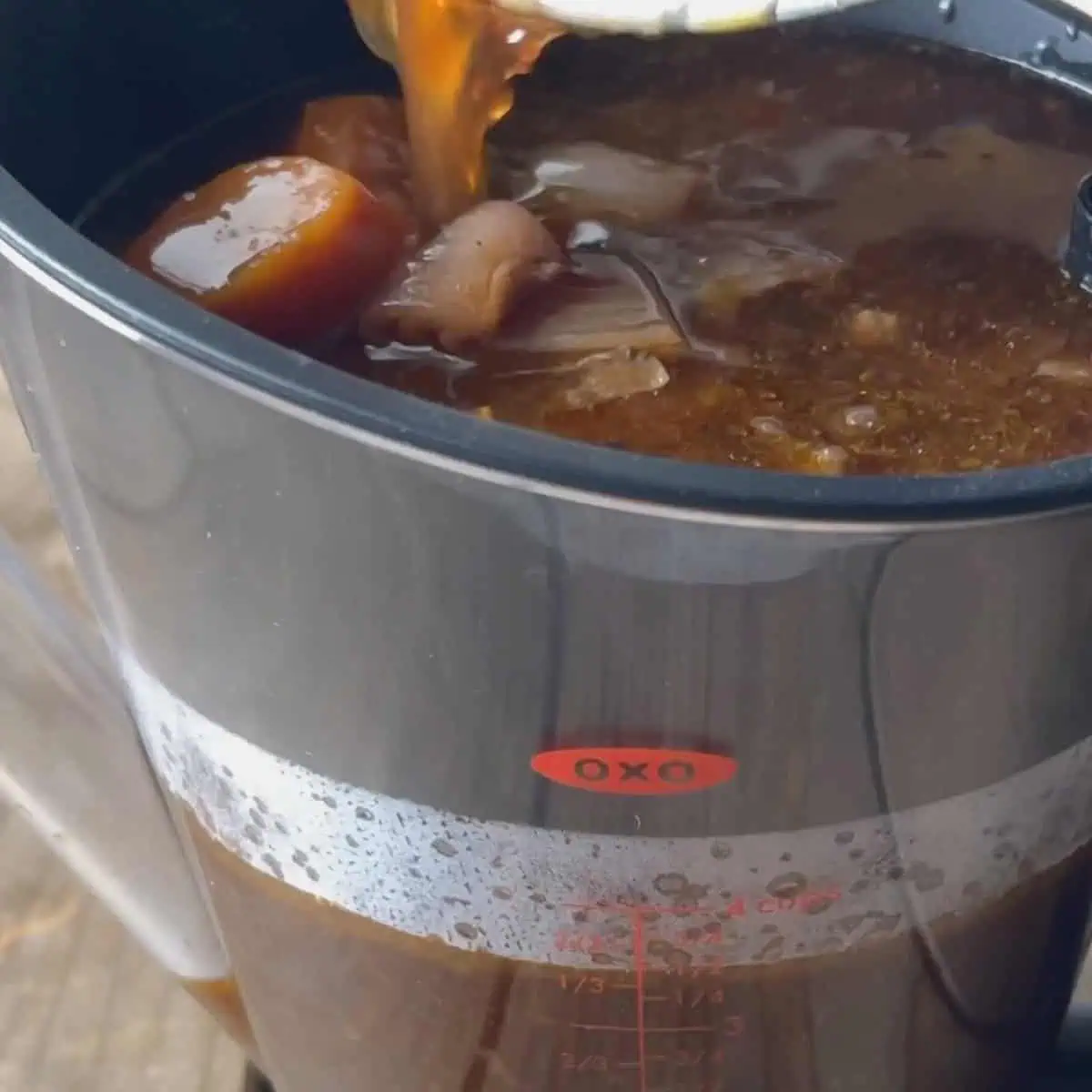 Broth from pressure cooker lamb shanks being poured into a fat separator with cooked onion and carrot pieces visible.