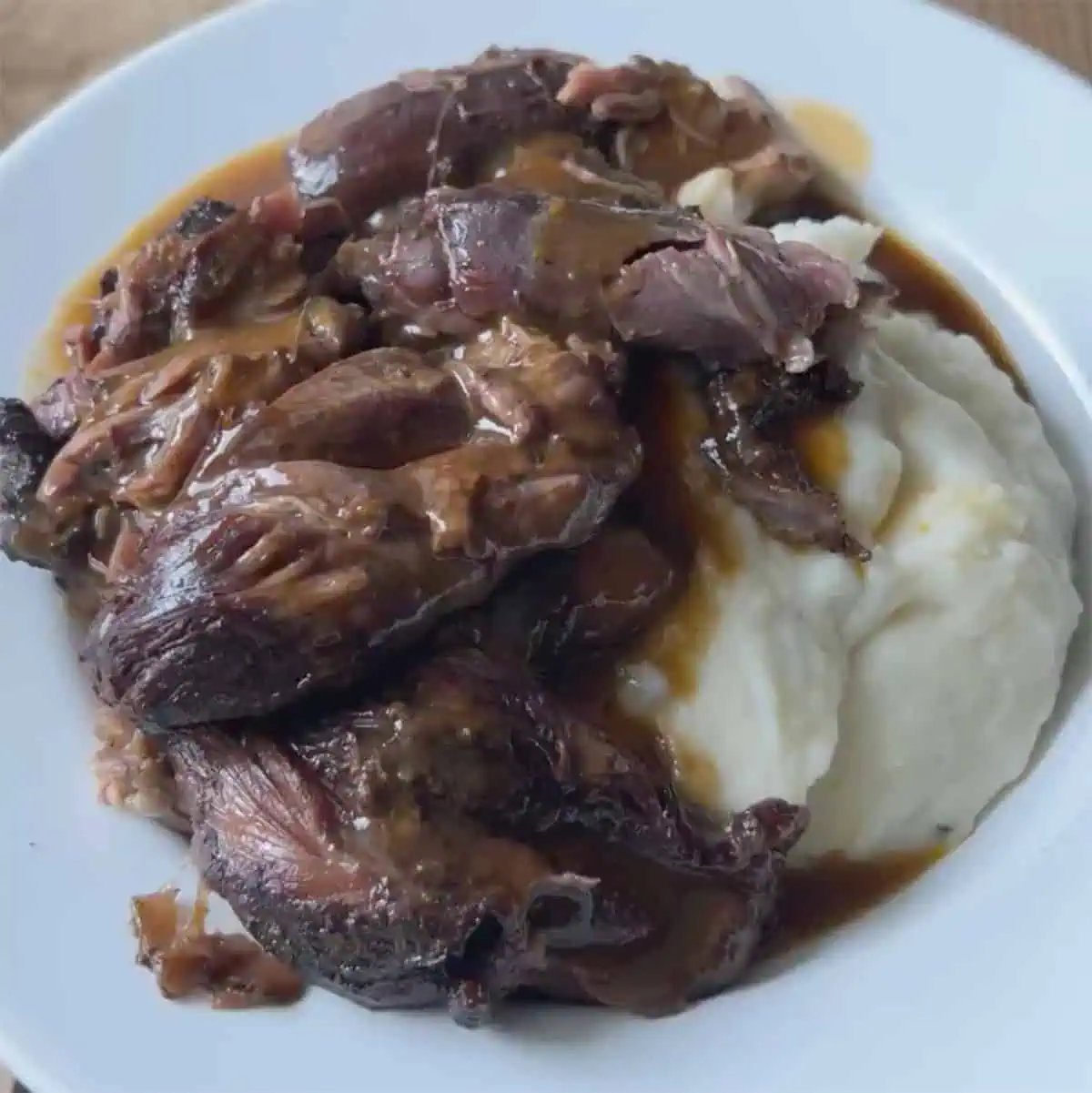Pressure cooker lamb shanks served over mashed potatoes with rich braising gravy on a white plate.